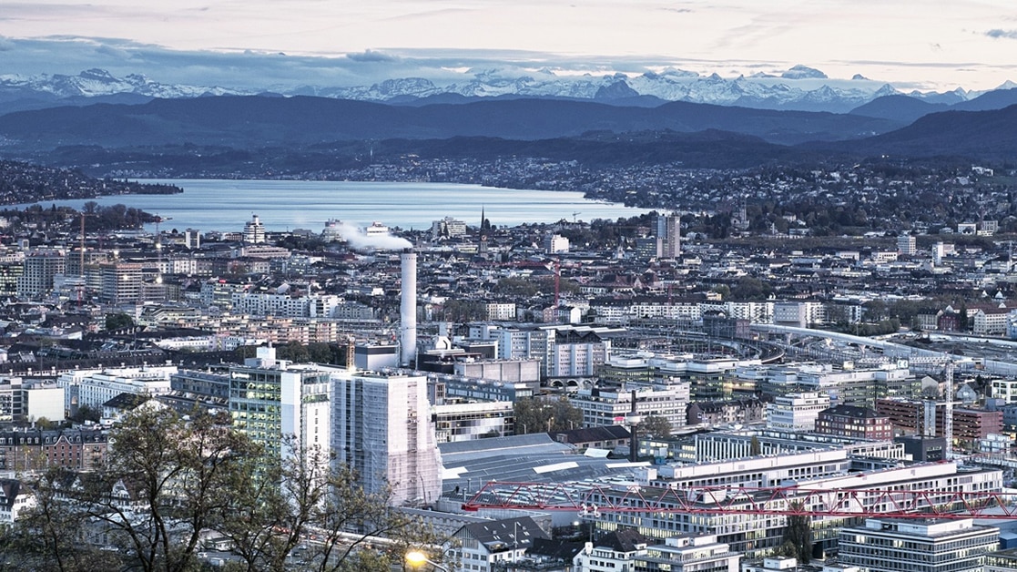 Blue toned cityscape with body of water and mountains in the background